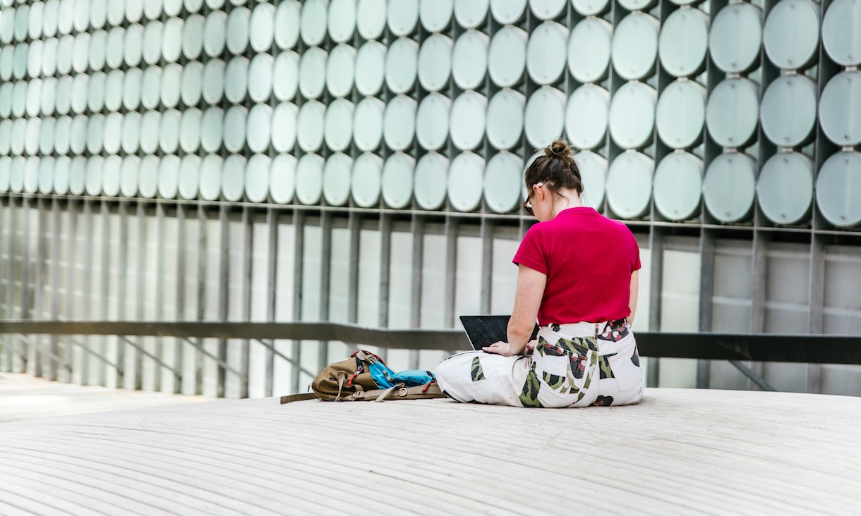 A student sits in front of an RMIT building, working on laptop.