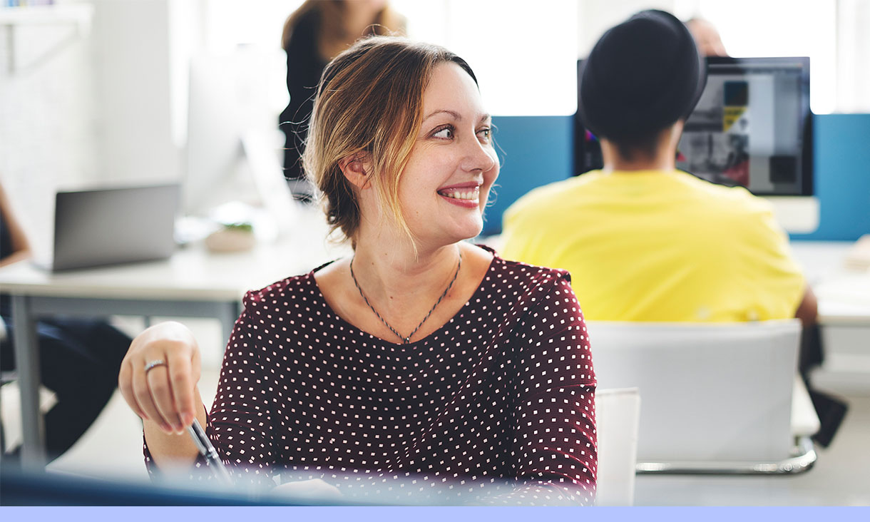 A woman smiles at her desk in an office.