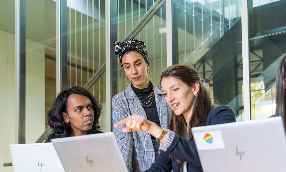 RMIT Business students stand about a computer discussing report results