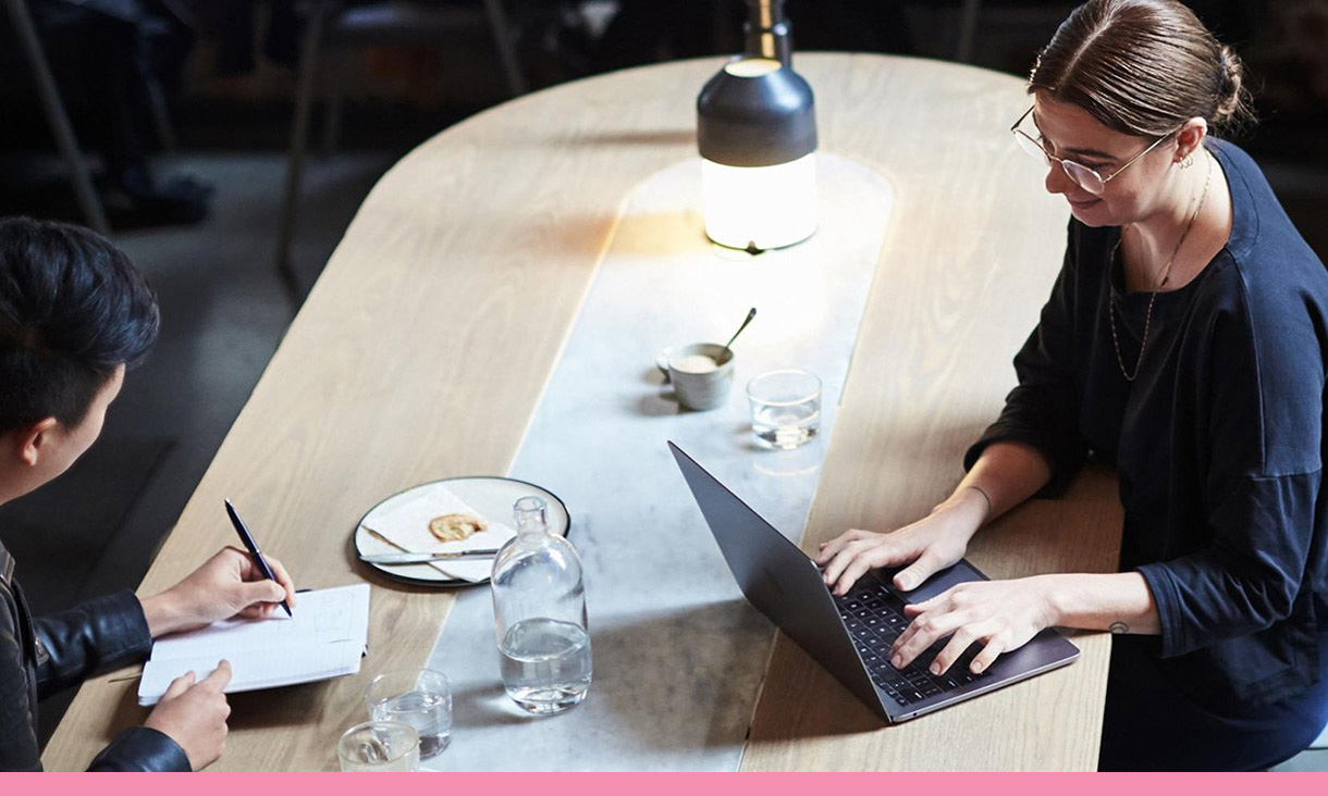 A woman types on her laptop while her coworker takes notes opposite her.