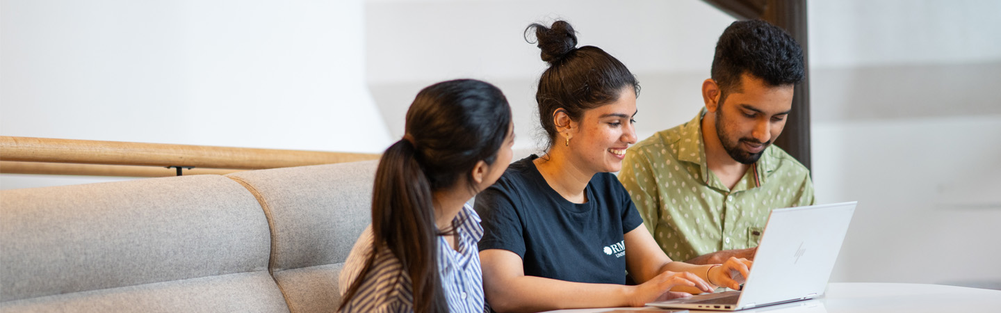 Three people on a couch looking at a laptop.