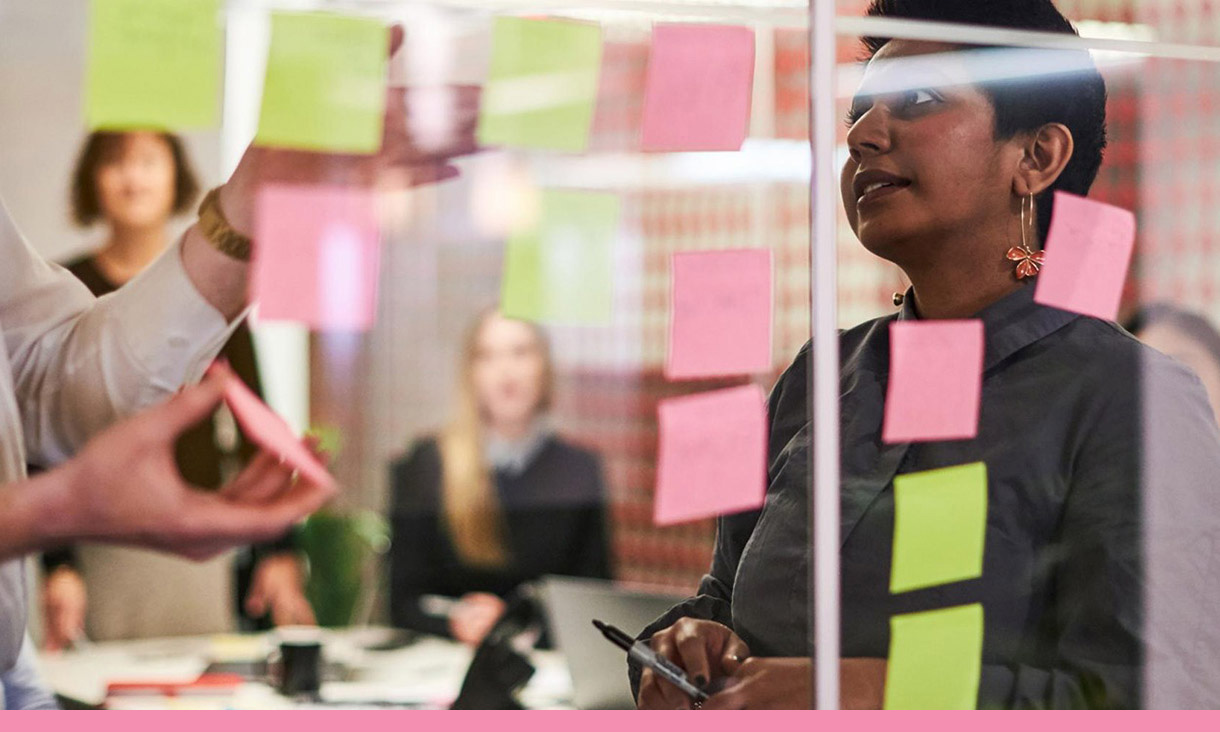 A group of coworkers make a wall of sticky notes.