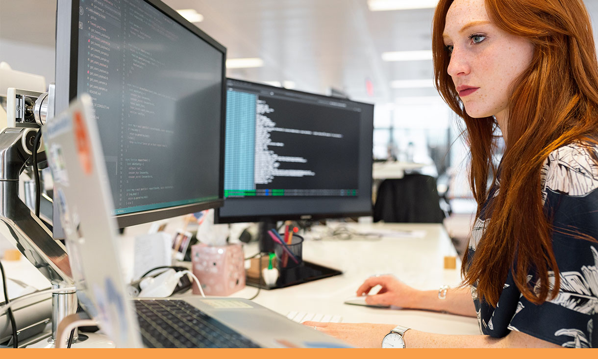 A woman looks at lines of code on a computer in an office.