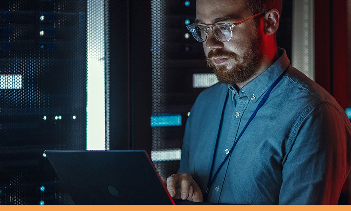 A man works on his laptop in a server room.