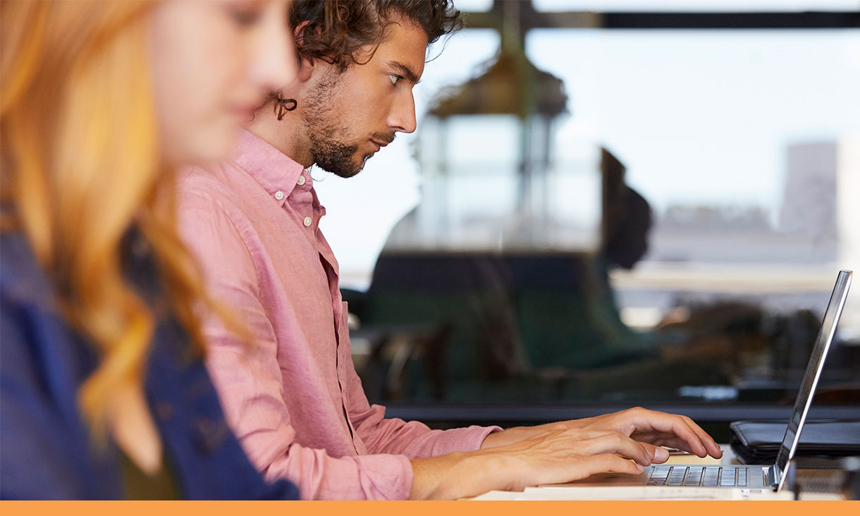 Two coworkers work side by side on their laptops.