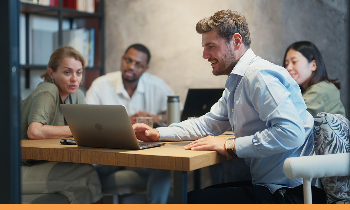 A man shows a group of coworkers something on his laptop in a meeting.