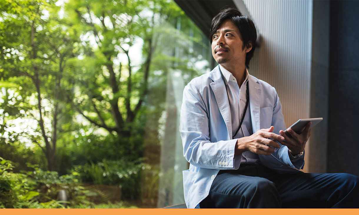 A man holding a tablet sits on a window seat and looks out the window.