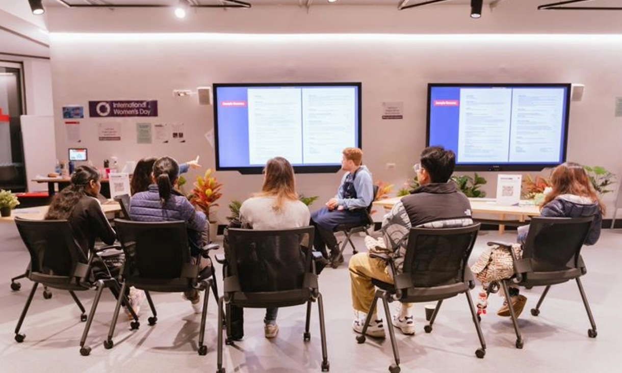 A group of people sitting on black chairs looking at a presentation.