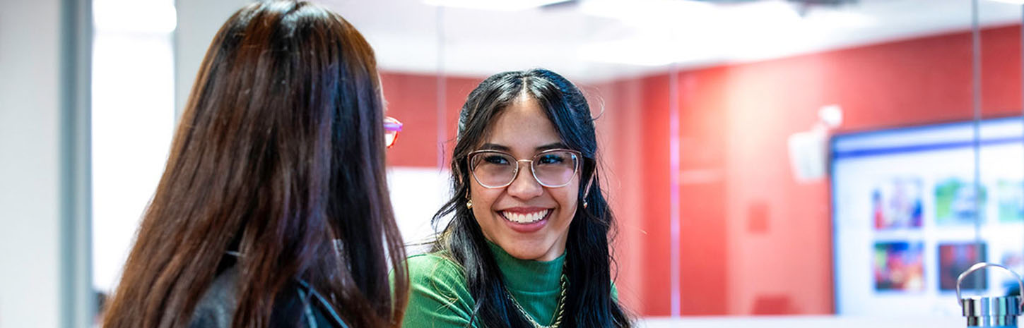 Two students on laptops, one facing away, one smiling at the other.