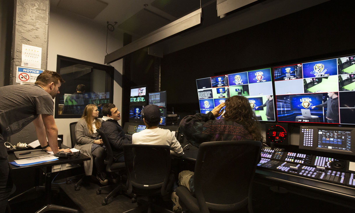 Two students seated looking at a media studio console.