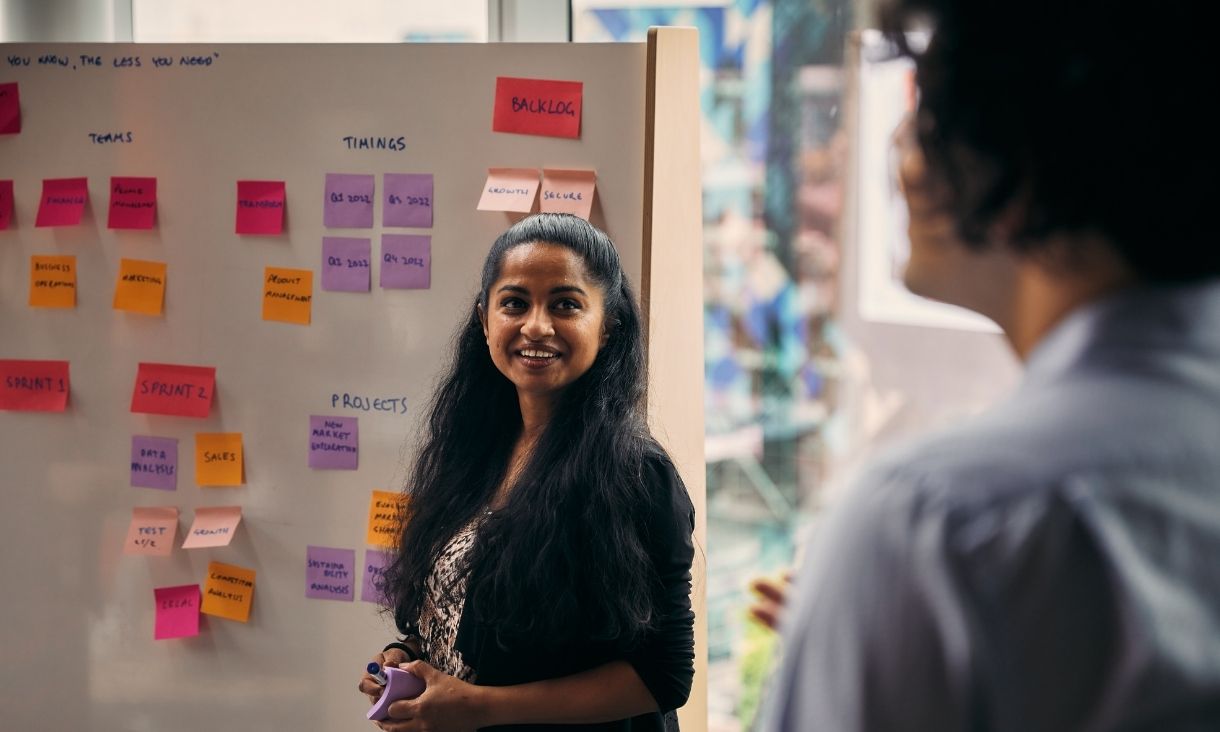 A woman stands in front of a whiteboard filled with Post-its.