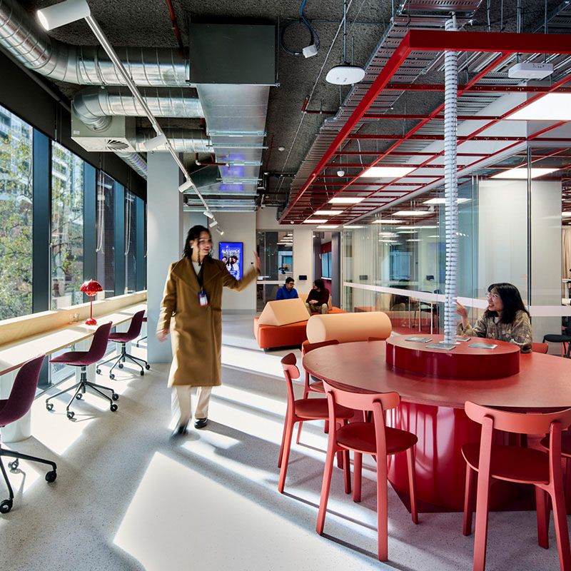 An interiro shot of a room with students sitting and one student standing, looking at another student.