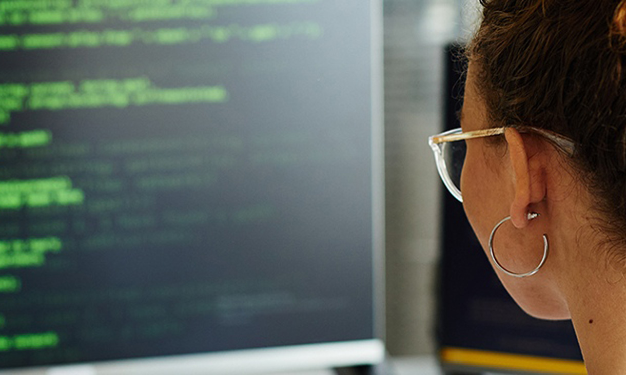 A woman sitting on a computer reading code. 