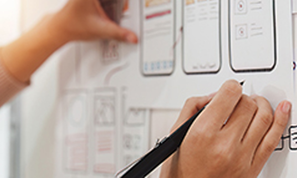 Someone drawing on a whiteboard that has images of an app in development on it. 