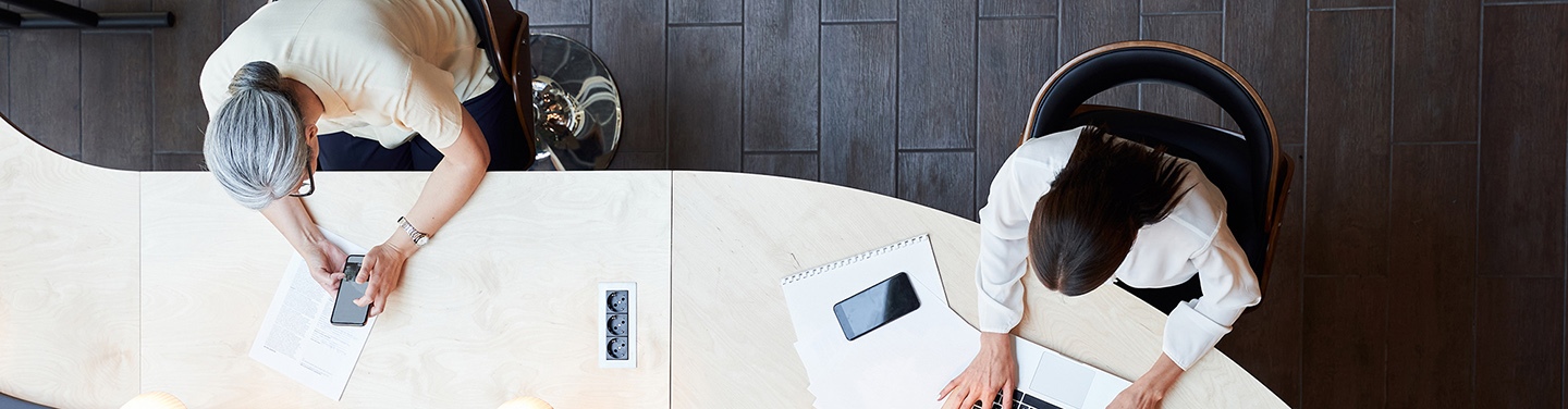 Birds-eye-view of two people working at a shared desk.