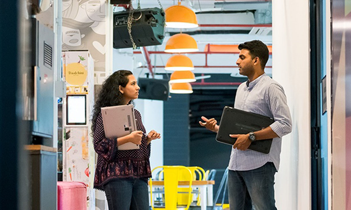 Two coworkers in conversation in an office hallway.