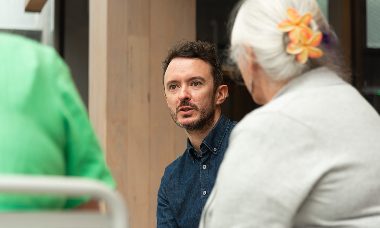 A man, centre of shot, talking to some people 